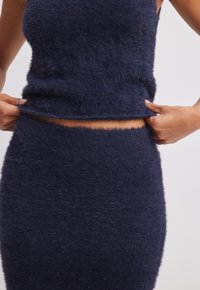Set in maglia fuzzy blu navy composto da due pezzi, con top corto senza maniche e gonna a vita alta, che mette in risalto la morbidezza della trama e i bordi invisibili.