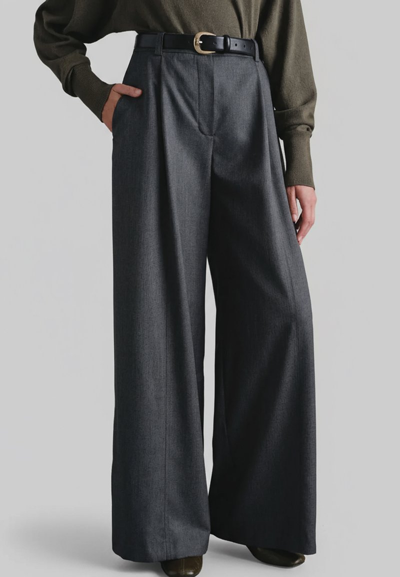 Szerokie spodnie z ciemnoszarej tkaniny o teksturowanym wykończeniu, z głębokimi plisami i czarnym paskiem z złotą klamrą.