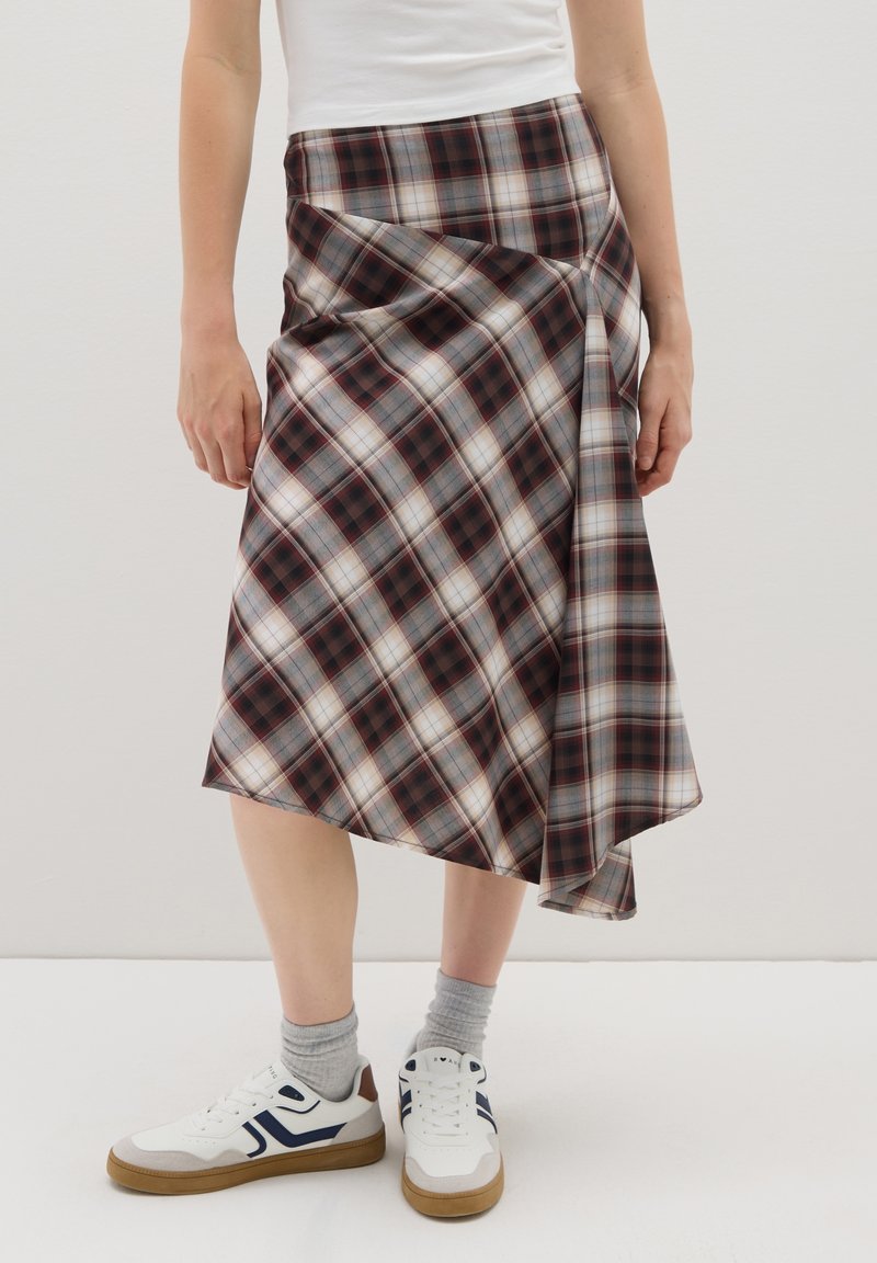 Persona vistiendo una falda midi de cuadros marrones y blancos, zapatillas blancas con detalles en azul marino y calcetines gris claro, sobre un fondo blanco.