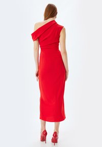 Vestido midi rojo de un solo hombro con una silueta ajustada y detalles drapeados. Combinado con zapatos de tacón rojos a juego. Tejido suave y elástico.