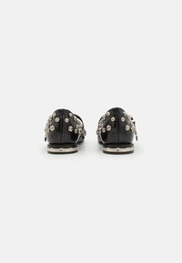 Zapatos de cuero negros con adornos de cristal, diseño de perfil bajo y suela texturizada negra, con un ribete metálico.