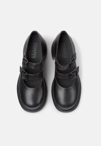 Scarpe in pelle nera con due fibbie, punta arrotondata e suola in gomma testurizzata. All'interno presenta una soletta nera con il logo "CAMPER".