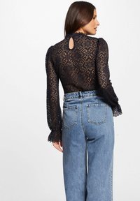 Blusa in pizzo navy a maniche lunghe, con motivo floreale e dettaglio a spacco sulla schiena, abbinata a jeans azzurri a vita alta.