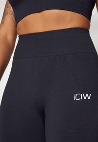 Crne tajice visokog struka od rastezljivog materijala. Imaju rebrasti pojas i mali bijeli logotip "ICIW" na lijevom bedru.