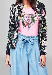 Zwarte bloemige bomberjack met een puffy textuur. Roze T-shirt met een decoratieve bloemige logo en lichtblauwe hoge taille, gestrikte broek.