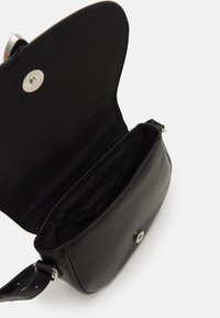 Černá kožená crossbody taška s otevřeným klopovým víkem, ukazující prázdný interiér a stříbrné magnetické zapínání na bílém pozadí.