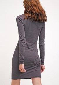 Robe grise à manches longues avec une silhouette ajustée, fabriquée en tissu doux, présentant une texture lisse et un design à mi-genoux.