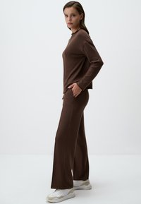 Brauner Strickpullover mit langen Ärmeln, runder Halslinie und seitlichem Schlitz; passende braune weitgeschnittene Hose mit Taschen und bequemer Passform.