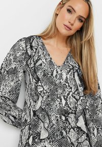 Blusa in stampa serpente bianca e nera con scollo a V, fronte arricciato e maniche lunghe. Il tessuto sembra setoso con una consistenza liscia.