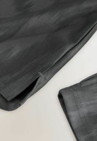 Dunkelgraue Stoffshorts mit glatter Textur, die genähte Nähte und eine Öffnung am Saum aufweisen. An der Seite gefalteter überschüssiger Stoff.