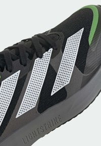 Scarpa da corsa nera in mesh con strisce perforate bianche e dettagli verdi. Presenta una intersuola grigia contrassegnata con "LIGHTSTRIKE" e lacci neri.