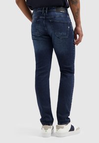 Donkerdenim jeans met een slim fit, met een subtiele vervaging, vijf zakken en een merkpatch op de tailleband. Geraadpleegd met witte sneakers.