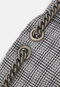 Černá a stříbrná kabelka s texturovaným materiálem, zdobená malými cvočky a masivním kovovým řetězem jako držadlem. Obsahuje detail s logem.