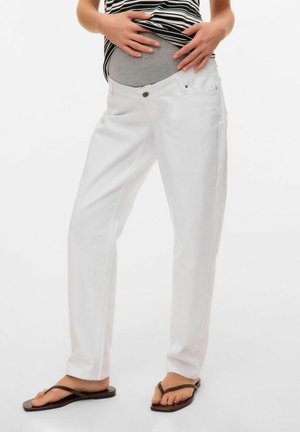 Osoba nosząca białe dżinsy ciążowe z elastycznym paskiem, lekko podniesioną bluzkę w paski i ciemne klapki na jednolitym tle.