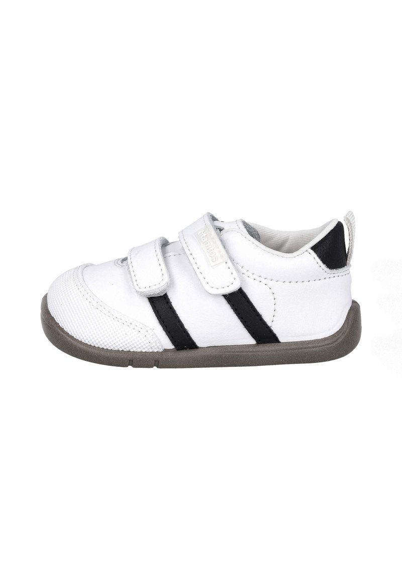 Zapatilla blanca con rayas negras, hecha de material sintético. Presenta una puntera texturizada, correas de Velcro y una suela de goma gris.