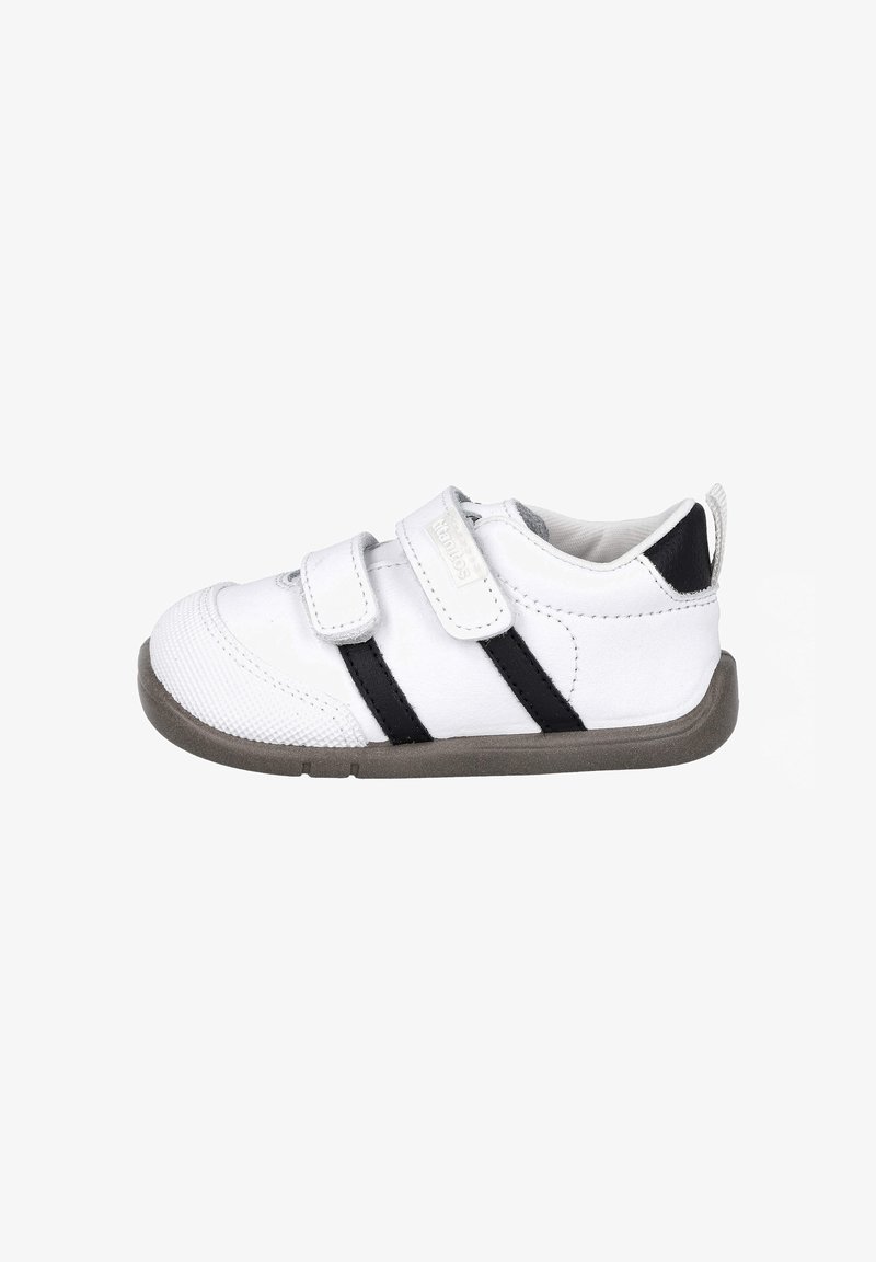 Zapatilla blanca con rayas negras, hecha de material sintético. Presenta una puntera texturizada, correas de Velcro y una suela de goma gris.