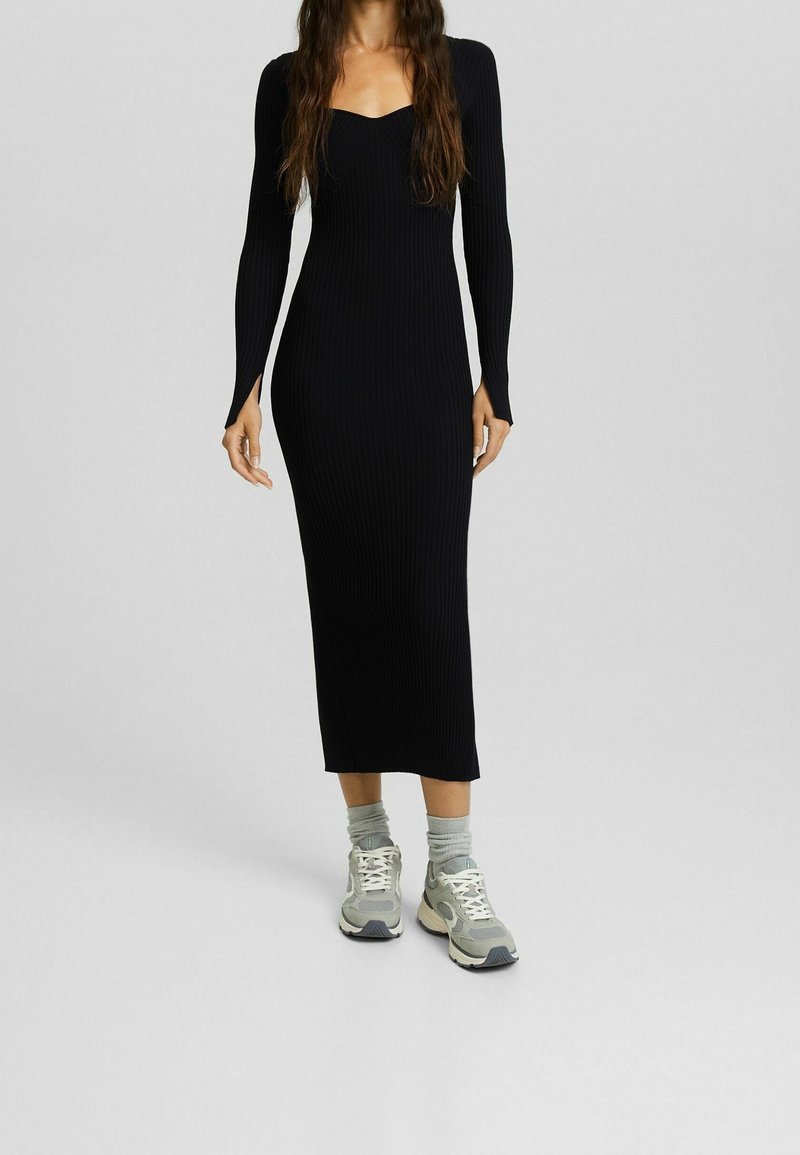 Femme portant une robe midi noire à manches longues côtelée, assortie à des chaussettes grises et des baskets épaisses grises et blanches.