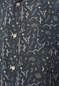 Camicia a maniche corte in tessuto nero con motivi a tema deserto in bianco e blu, con chiusura a bottoni e taschino applicato.