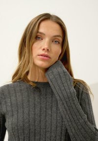 Szary sweter z ryżu o długich rękawach i okrągłym dekolcie, charakteryzujący się miękką teksturą oraz dopasowaną sylwetką.