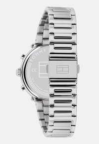 Montre en acier inoxydable argenté avec un bracelet à maillons poli, un cadran rond et un détail de logo au dos, mettant en valeur son design et sa finition élégants.
