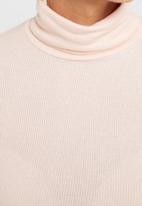 Hellrosa Rollkragenpullover aus geripptem Stoff, mit einem engen Kragen und glatter Textur. Ideal zum Layering in kühler Wetterlage.