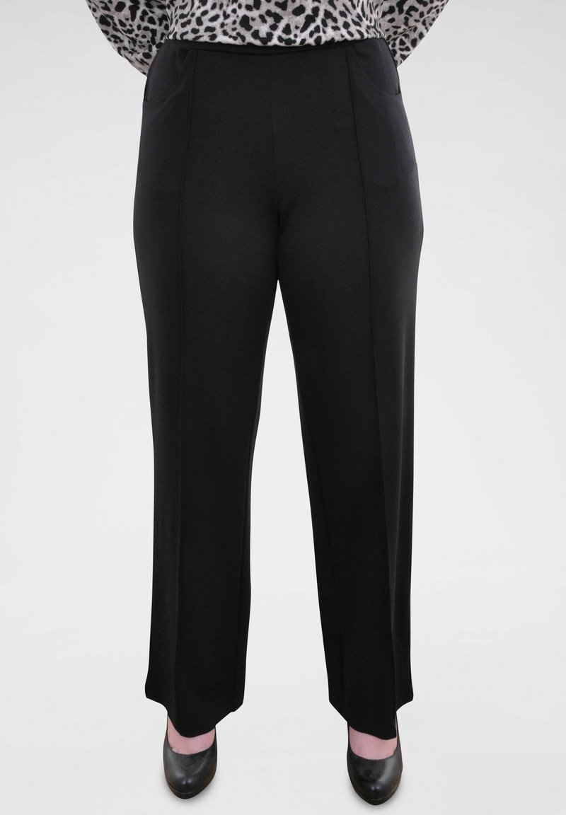 Zwarte, wijde broek van gladde stof, met twee voorzakken en een platte taille, gedragen met zwarte hakken.