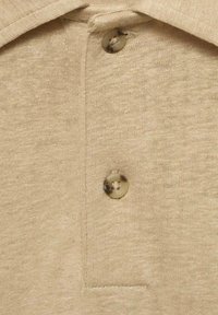 Béžová polo tričko s límečkem a dvěma knoflíky. Hladká tkanina má jemnou strukturu, což podtrhuje neformální design.