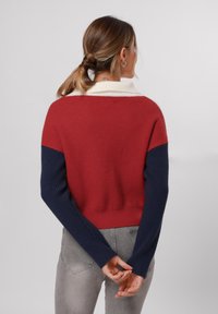 Maglione a blocchi di colore rosso e blu navy con una trama a coste e colletto bianco. Presenta maniche lunghe e un design cropped, con cucitura a vista sul retro.