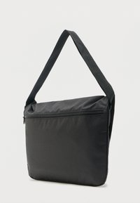 Μαύρη ορθογώνια τσάντα ώμου με επένδυση και κλείσιμο με φερμουάρ σε απλό ανοιχτό φόντο.