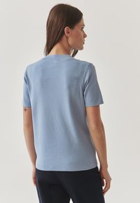Světle modrý top s krátkým rukávem a kulatým výstřihem, jemnou texturou a uvolněným střihem, s minimalistickým designem bez vzorů.
