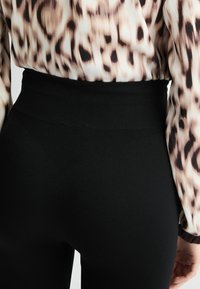 Leggins negros de tiro alto con una cinturilla texturizada, diseño ajustado y tejido suave. La parte superior presenta un patrón de leopardo fluido.