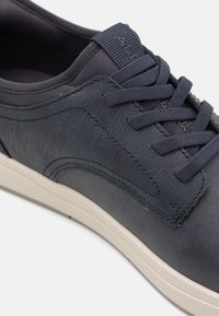 Dark blue sneaker featuring a textured upper, smooth accents, and a cream-colored sole. Includes standard lace design and padded collar.