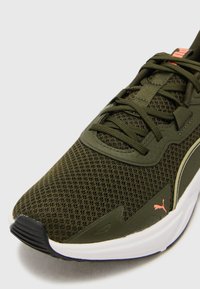 Green mesh athletic shoe with textured upper, black toe cap, white sole, and subtle orange branding. Features laces and padded tongue.
