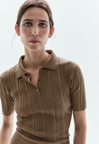 Polo shirt marron côtelé à manches courtes, doté d'un col et de trois boutons, en tissu texturé avec des rayures verticales.