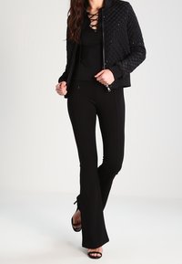 Czarna pikowana kurtka bomberka z zapięciem na zamek, zestawiona z dopasowanym czarnym topem i rozszerzanymi czarnymi spodniami. Sandały na obcasie w czarnym kolorze dopełniają całość.