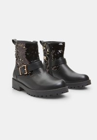 Botas negras hasta el tobillo con una parte delantera de cuero liso y una parte trasera decorada con lentejuelas. Cuentan con una correa con hebilla y una suela resistente para tracción.
