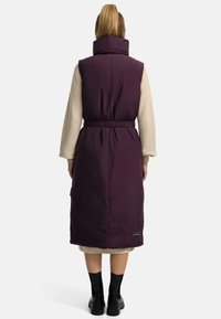 Gilet imbottito senza maniche color bordeaux con colletto alto, vita elastica e tasche laterali, caratterizzato da una texture liscia e un design che arriva fino al ginocchio.