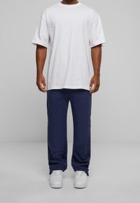 Weißes Baumwoll-T-Shirt mit kurzen Ärmeln, kombiniert mit navyblauen, locker sitzenden Jogginghosen. Weiße Sneakers runden das Outfit ab.