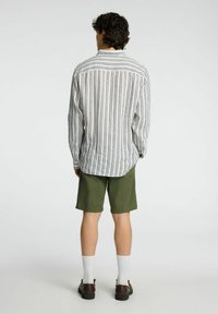 Camicia a maniche lunghe a righe in bianco, blu navy e beige, abbinata a pantaloni corti verde oliva. Presenta una vestibilità comoda e particolare sul retro.