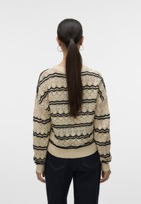 Maglione lavorato a maglia color crema con strisce zigzag nere, caratterizzato da un design a rete testurizzato e polsini e orlo a coste, mostrato di lato.