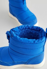 Blaue isolierte Stiefel mit glattem Außenbereich, gepolstertem Design und textilartigem Innenfutter. Verfügt über weiße Gummisohlen und einen gerafften Kragen.