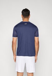 Αθλητική μπλούζα σε ναυτικό μπλε χρώμα με κοντά μανίκια, κυκλική λαιμόκοψη και λευκές λεπτομέρειες, κατασκευασμένη από υλικό που απομακρύνει την υγρασία.