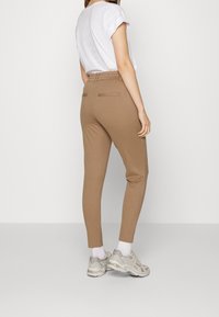 Brown fitted trousers with a smooth texture and elastic waistband, paired with a white short-sleeve shirt and light gray athletic shoes.