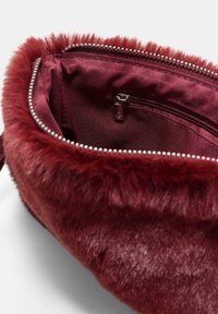 Notranjost burgundske umetne krzna torbice je gladka podloga. Ima žep na zadrgo in kovinsko zadrgo ob robu.