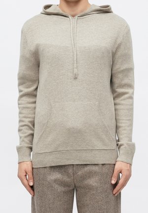 Beiger gestrickter Hoodie mit Fronttasche, Kordelzügen und gerippten Bündchen, kombiniert mit strukturierten braunen Hosen.