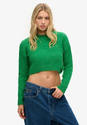 Green cropped sweater with long sleeves, textured material, and ribbed hem. Paired with loose-fitting blue denim jeans.