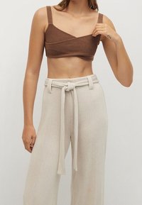 Top court marron avec de fines bretelles, présentant un design croisé. Associé à un pantalon large crème taille haute avec une ceinture nouée. Texture lisse.