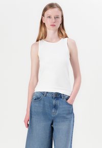 Hvit ermeløs tanktop i et mykt stoff, satt sammen med lyseblå vide jeans. Jeansene har frontlommer og knappelukking.