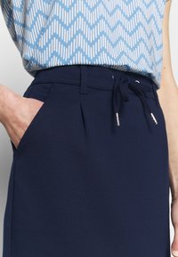 Navy blue jogginghousut, joissa on naru vyötäröllä, sivutaskut ja laskostusdetail, yhdistettynä kuvioituun vaaleansiniseen paitaan.