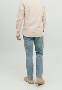 Vaaleanpunainen pitkähihainen paita, siniset farkut, vaaleat kengät. Farkuissa on kulunut ilme, paidassa on nappikaulus yksityiskohtia.